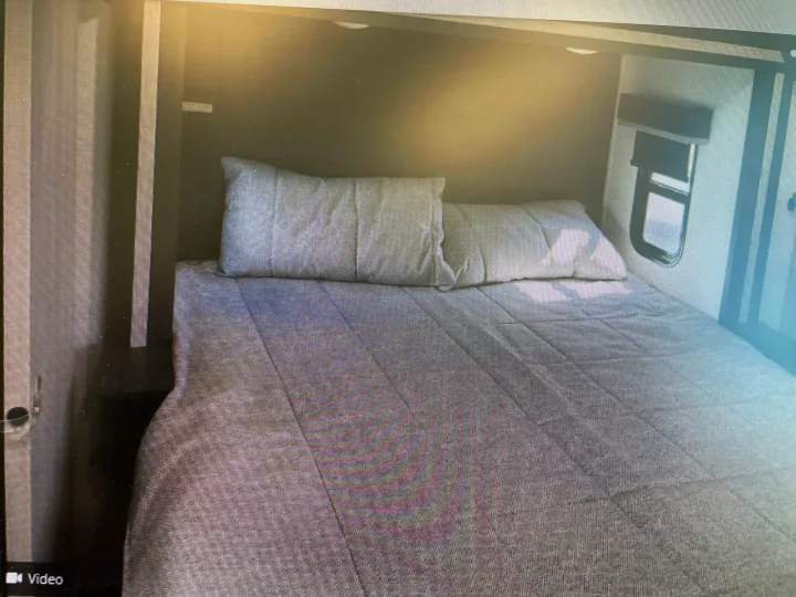RV rental bedroom view: a neatly made bed with two grey pillows and a quilted comforter in a compact RV interior.. Keystone Fuzion 2021