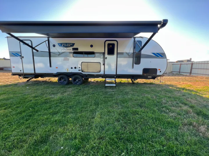 This RV rental, a white travel trailer with an extended awning, is parked on grass under a clear sky.. Forest River Salem cruise lite 2023