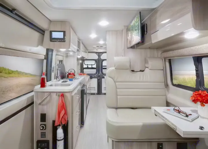 A bright, modern RV rental interior reveals a kitchen, dining/lounge area with TV, ready for your next adventure.. Thor Sequence 2022