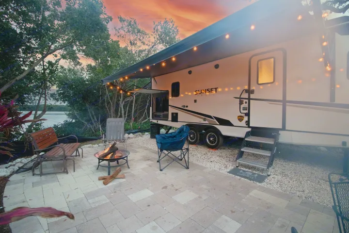 Cozy RV rental campsite at sunset, featuring an illuminated RV, a crackling fire pit, and waterfront views.. Crossroads RV Sunset Trail Super Lite 2022