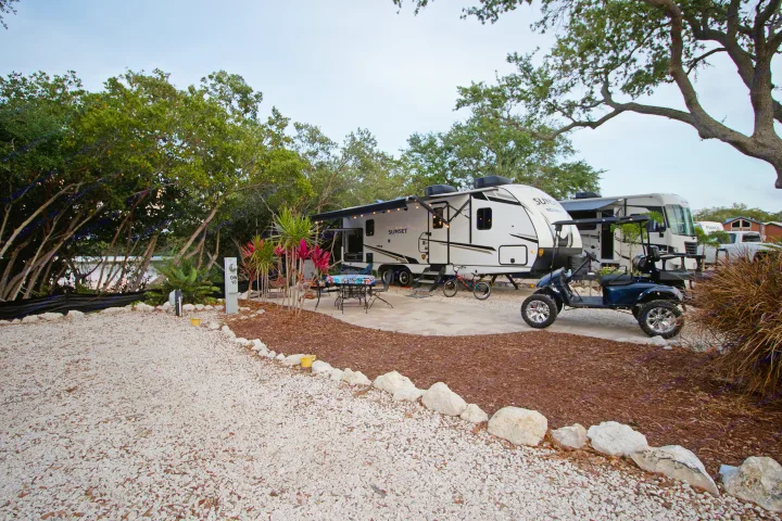 Waterfront RV rental site featuring a travel trailer, golf cart, and outdoor living area amidst lush landscaping.. Crossroads RV Sunset Trail Super Lite 2022