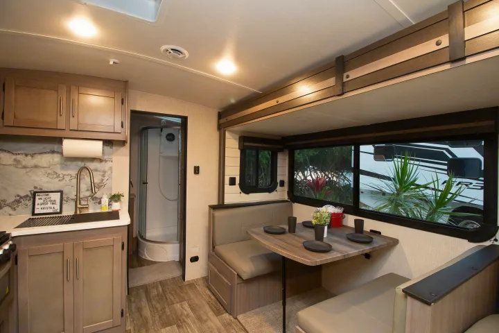 Cozy RV rental interior view of the kitchen, complete with sink, adjacent dinette seating, and a compact bathroom.. Crossroads RV Sunset Trail Super Lite 2022