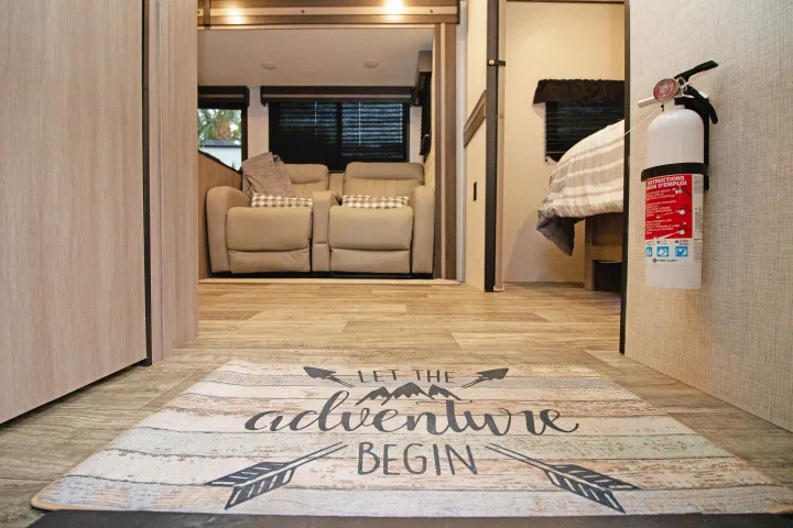 Cozy RV rental interior with "adventure" mat, recliners, bed, and fire extinguisher for a safe journey.. Crossroads RV Sunset Trail Super Lite 2022