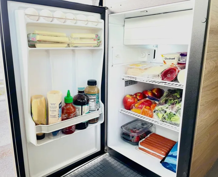 RV rental fridge packed with string cheese, sauces, deli meats, yogurt, apples, hot dogs, and fresh produce for easy travel meals.. Winnebago SOLIS 59 PX 2023
