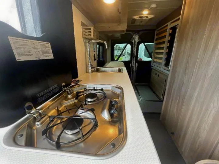 Inside an RV rental: a compact kitchen area with a two-burner stove, sink, and counter space for mobile living.. Winnebago SOLIS 59 PX 2023
