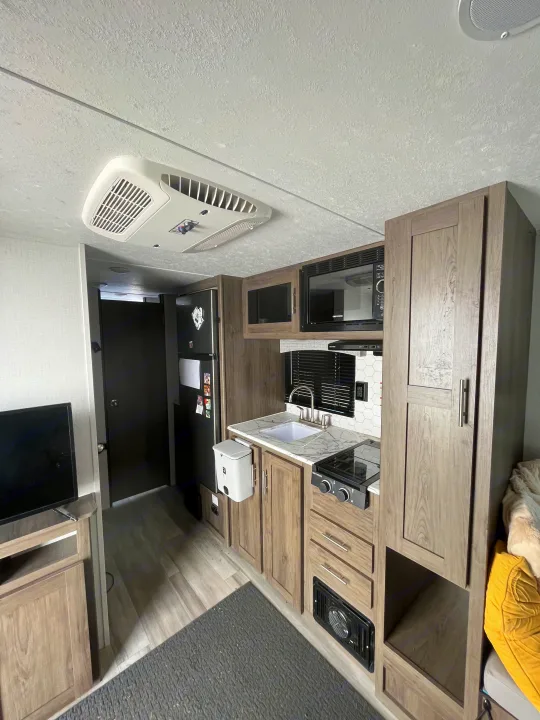 Well-appointed RV rental interior showing a modern kitchen with sink, stovetop, microwave, fridge, plus an overhead AC unit.. Forest River Coachman Clipper 2022