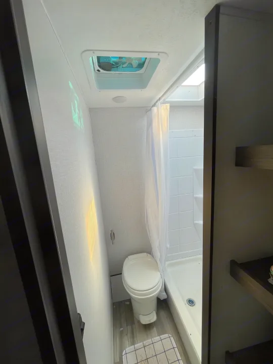 Efficient RV rental bathroom. Features a compact toilet, shower with curtain, and sky-lighted ceiling vent. Bright natural light.. Forest River Coachman Clipper 2022