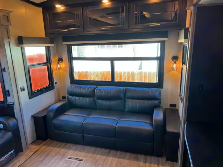 Cozy RV rental living area featuring a dark leather reclining sofa, large windows, overhead cabinets, and soft sconce lighting.. Jayco Pinnacle 2022