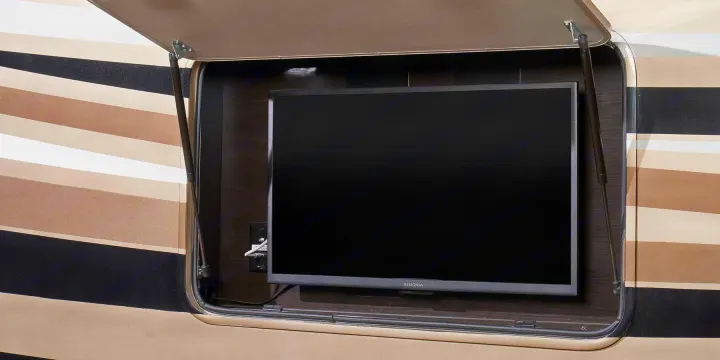 An open RV rental compartment reveals an Insignia outdoor TV, perfect for entertainment on your travels, with gas struts holding the door.. Jayco Pinnacle 2022