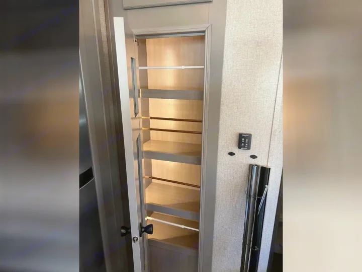 RV rental interior: an open, illuminated pantry with multiple pull-out shelves, ideal for compact storage beside a refrigerator.. Jayco Pinnacle 2022