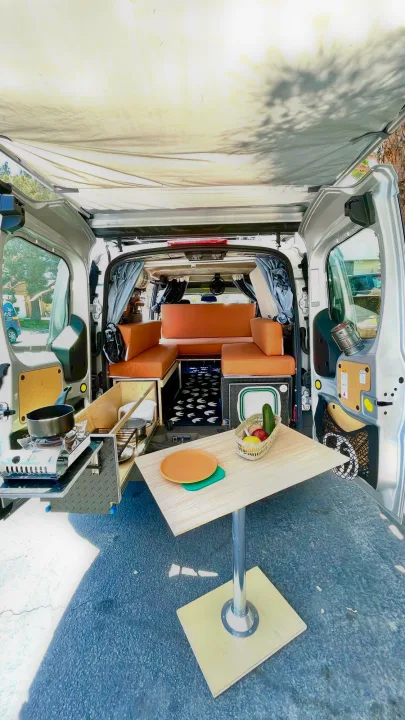 RV rental: Compact camper van interior with convertible seating, kitchen pull-out, and outdoor table under an awning.. Ford transit connect 2022