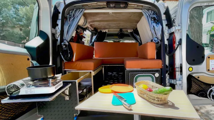 Compact camper van interior with cooking setup, dining table, and orange seating. Perfect for your next rv rental road trip.. Ford transit connect 2022