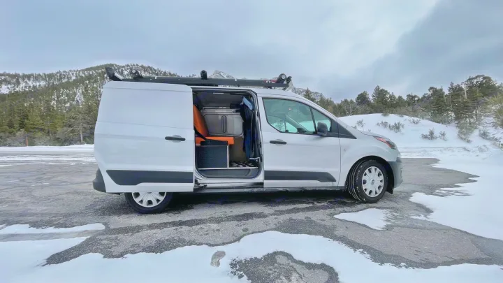RV rental ready for winter adventures! See this white camper van with custom interior in a snowy mountain landscape.. Ford transit connect 2022