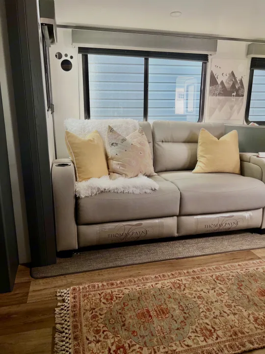 RV rental's inviting living space: comfortable grey sofa, decorative pillows, fluffy throw, patterned rug, large windows.. Keystone Bullet Ultra Lite 2023