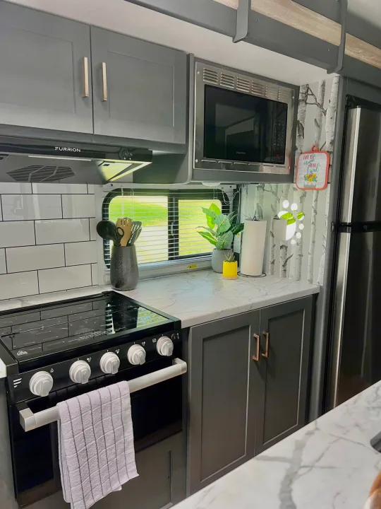 Sleek RV rental kitchen with gray cabinets, marble counters, subway tile backsplash, and Furrion appliances.. Keystone Bullet Ultra Lite 2023