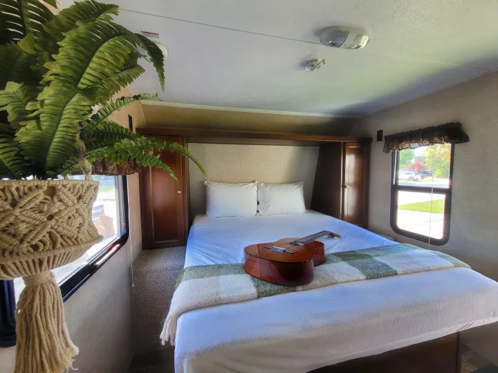 Serene RV rental bedroom: comfy bed, classical guitar, and a hanging fern plant by the window.. Keystone RV Hideout LHS 2016