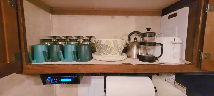An organized RV rental kitchen cabinet with mugs, glasses, kettle, French press, toaster, plates, and cutting board.. Keystone RV Hideout LHS 2016