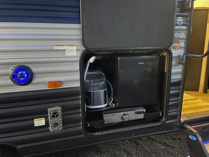 RV rental's outdoor kitchen, featuring a Hotpoint fridge, ice maker, Greystone cooktop, and blue-lit speaker for camping.. Forest River Cherokee Grey Wolf 2022