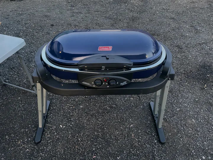 A blue Coleman RoadTrip portable grill, perfect for outdoor cooking during an RV rental trip.. Forest River Cherokee Grey Wolf 2022