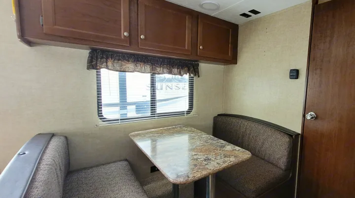 RV rental dinette area: upholstered bench seats, a patterned table, overhead cabinets, and a window with blinds.. Keystone RV Hideout LHS 2016