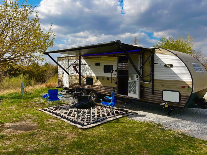 This RV rental is perfectly set up at a sunny campsite, featuring an extended awning with blue lights, chairs, and an outdoor mat.. Forest River Forrest River Cherokee Patriot Edition 26DBH 2015