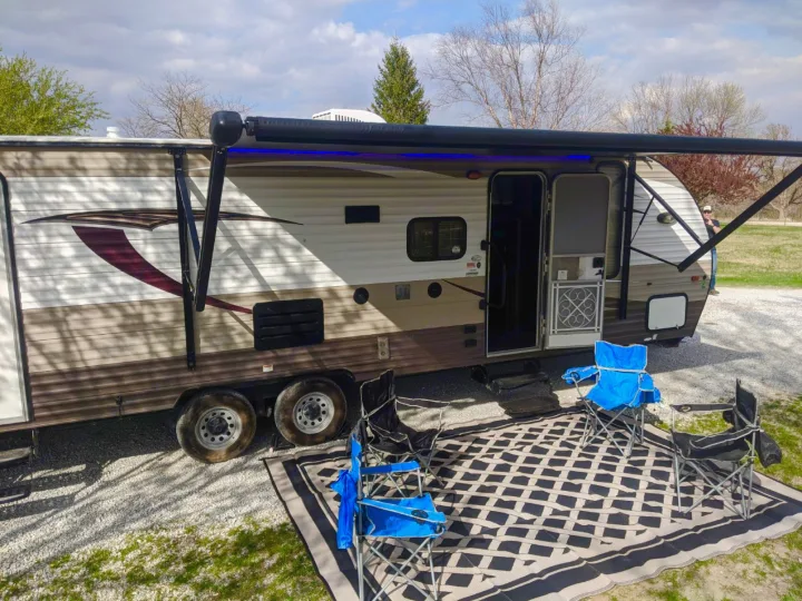 Enjoying an RV rental setup: a travel trailer with an illuminated awning, outdoor rug, and camping chairs.. Forest River Forrest River Cherokee Patriot Edition 26DBH 2015