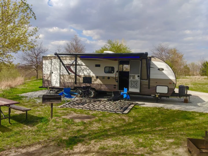 Campsite scene featuring an RV rental with awning extended, blue lights, chairs, picnic table, and grill.. Forest River Forrest River Cherokee Patriot Edition 26DBH 2015