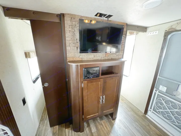 Cozy RV rental interior with a TV mounted on a stone wall, entertainment unit, and spacious layout. Ideal for travel.. Forest River Forrest River Cherokee Patriot Edition 26DBH 2015