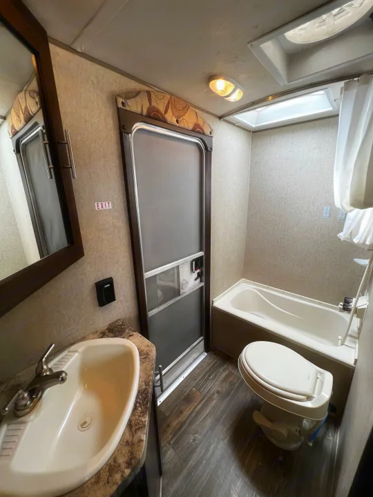 Compact RV rental bathroom with sink, toilet, tub, mirror, and an "EXIT" door. Ideal for your next RV adventure.. Forest River Forrest River Cherokee Patriot Edition 26DBH 2015