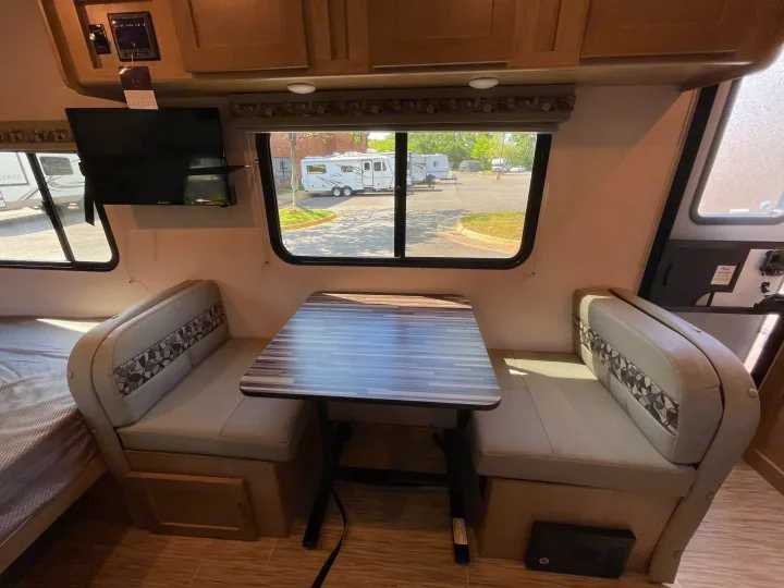 RV rental interior: dinette with table & patterned bench seats, TV, and bed. Window view of other RVs.. Forest River R-Pod 2021