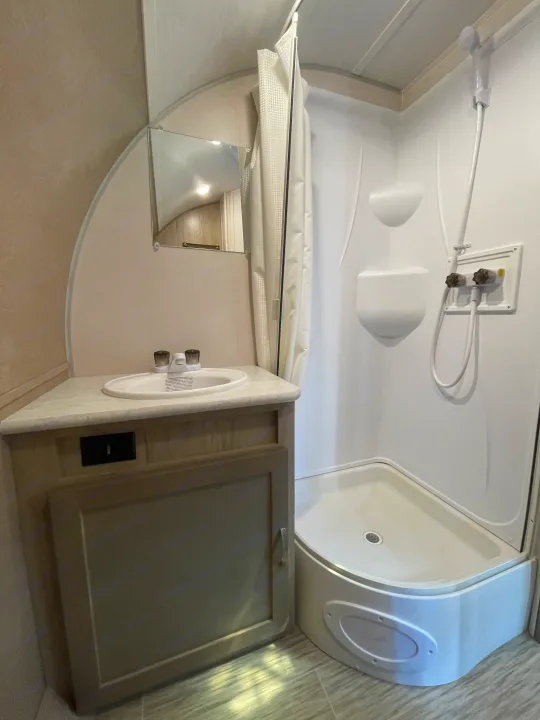 RV rental bathroom features a small sink, vanity, mirror, and a compact white shower with fixtures and curtain.. Forest River R-Pod 2021