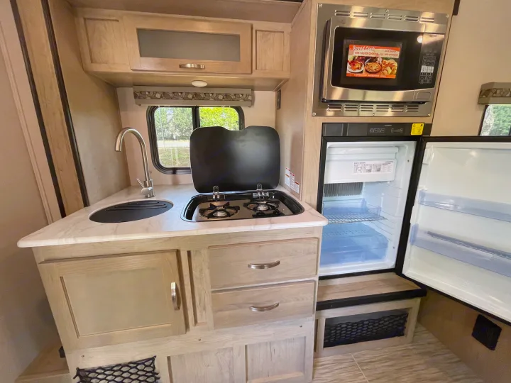 RV rental: Compact kitchen with sink, two-burner stove, microwave, and open refrigerator. Features light wood cabinets.. Forest River R-Pod 2021
