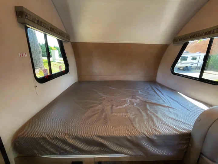 RV rental bed area with a comfortable mattress, soft headboard, and dual windows offering outdoor views. Find comfort on the road.. Forest River R-Pod 2021