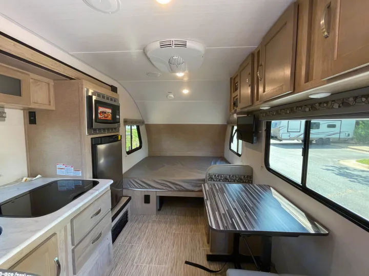 Well-equipped RV rental interior: kitchen with microwave/fridge, rear bed, and dinette. Brightly lit and compact.. Forest River R-Pod 2021