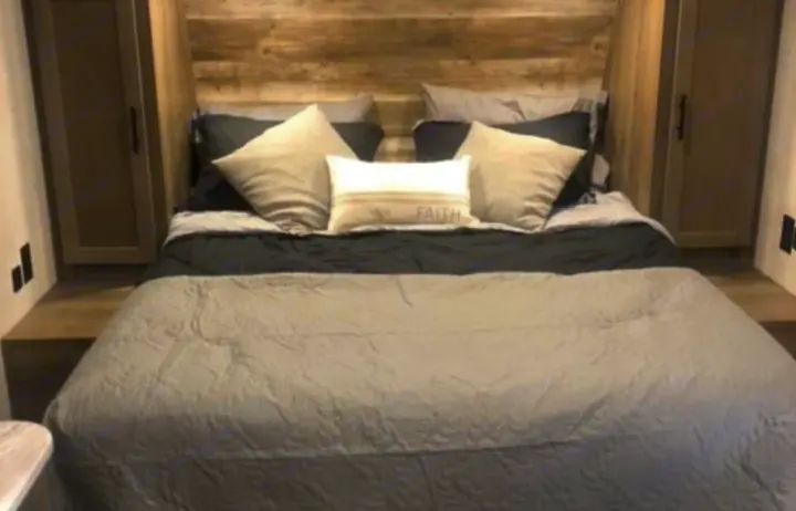 Cozy RV rental bedroom featuring a comfy bed with grey and black bedding, built-in storage, and a wooden headboard.. Gulf Stream Ameri-Lite 2022