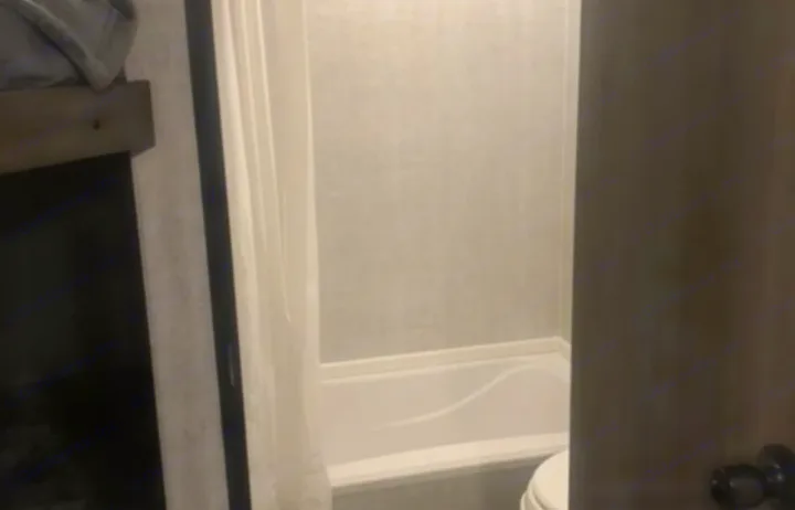 RV rental interior: A compact bathroom with a small tub/shower and toilet, seen from a living area with a bunk bed.. Gulf Stream Ameri-Lite 2022