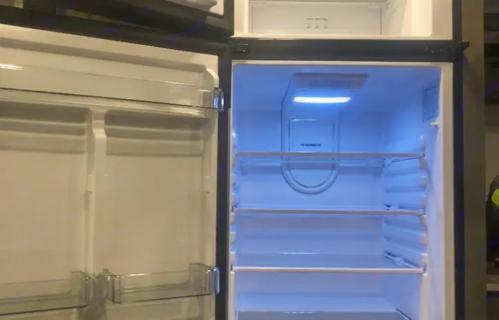 This RV rental features a clean, empty Dometic refrigerator with blue interior lighting, perfect for your trip.. Gulf Stream Ameri-Lite 2022