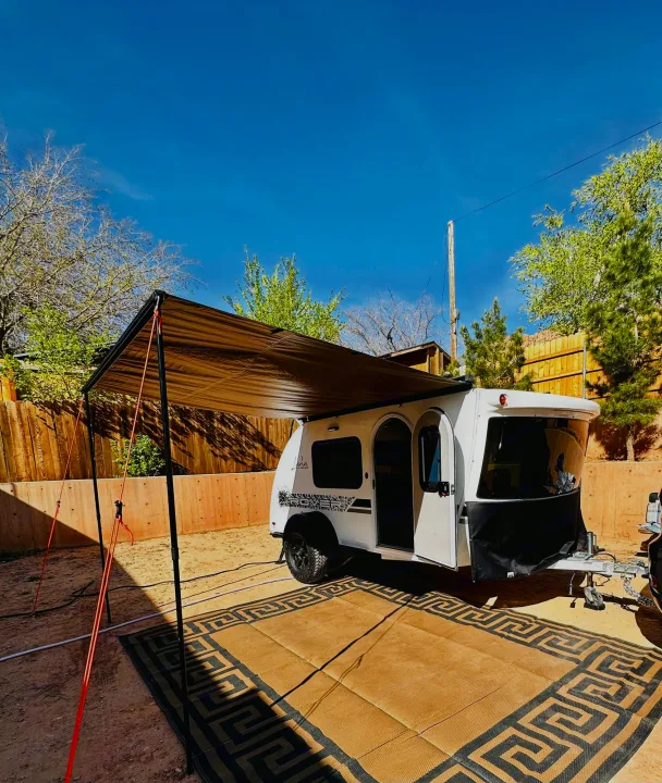 White teardrop RV rental showcasing its setup with a brown awning and patterned outdoor mat at a campsite.. InTech RV InTech RV Trailer 2021