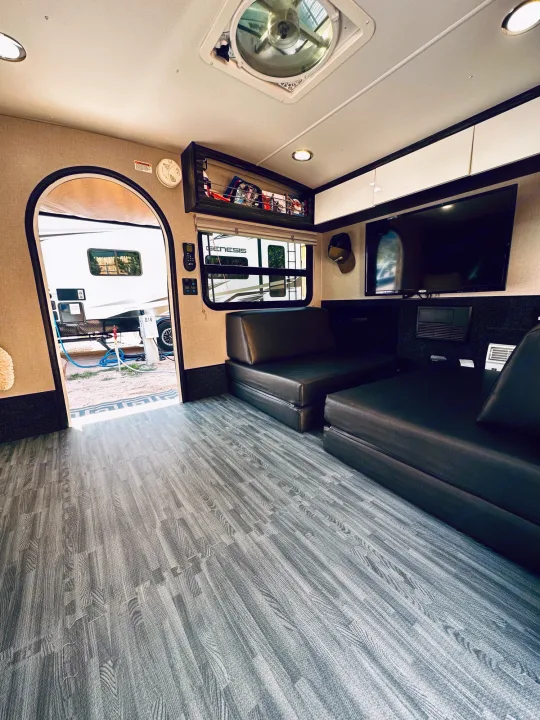Tour this rv rental's interior: grey wood-look flooring, two dark sofa beds, a TV, and an open archway revealing the campsite.. InTech RV InTech RV Trailer 2021