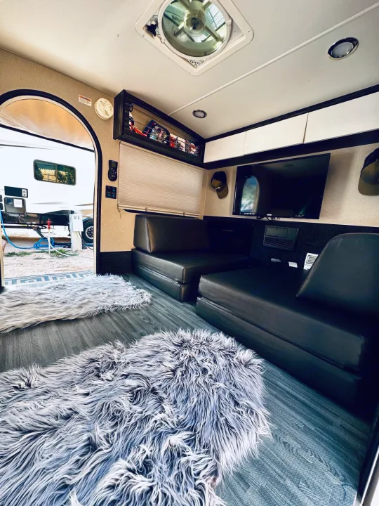 Inside a comfy rv rental, featuring black modular sofas, soft gray rugs, TV, and outdoor view.. InTech RV InTech RV Trailer 2021