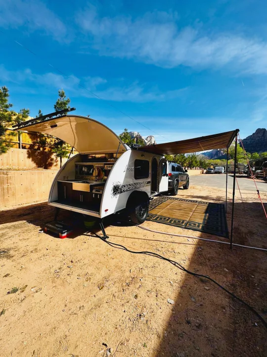 Enjoying the outdoors with an RV rental! A teardrop trailer with an open kitchen and awning is set up at a scenic campsite.. InTech RV InTech RV Trailer 2021
