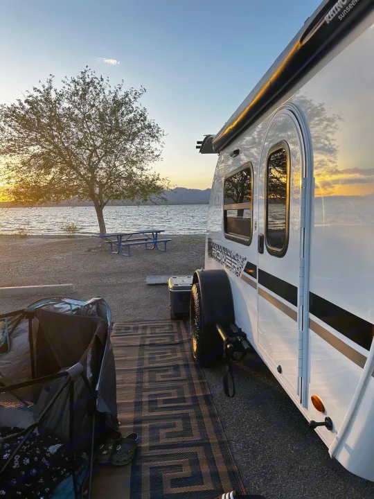 RV rental by a lake at sunset. A white camper, tree, and picnic table make for a peaceful waterfront camping spot.. InTech RV InTech RV Trailer 2021
