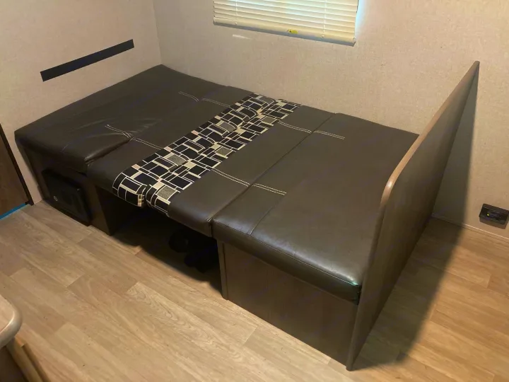 Compact RV rental interior featuring a versatile sofa bed with patterned accents, light wood flooring, and window blinds.. Dutchmen Coleman Lantern LT 2019
