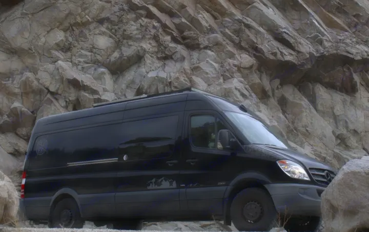 Black Sprinter van RV rental, ready for off-road adventure by a rocky cliff.. Mercedes Sprinter 2012