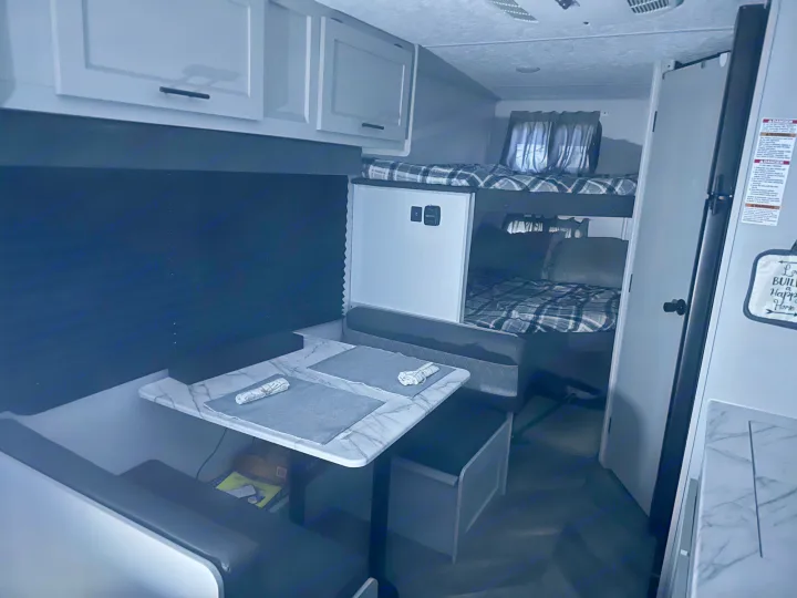 Modern rv rental interior showing bunk beds, a dinette setup, and kitchen area with a refrigerator.. Forest River Salem FSX PLATINUM 2021