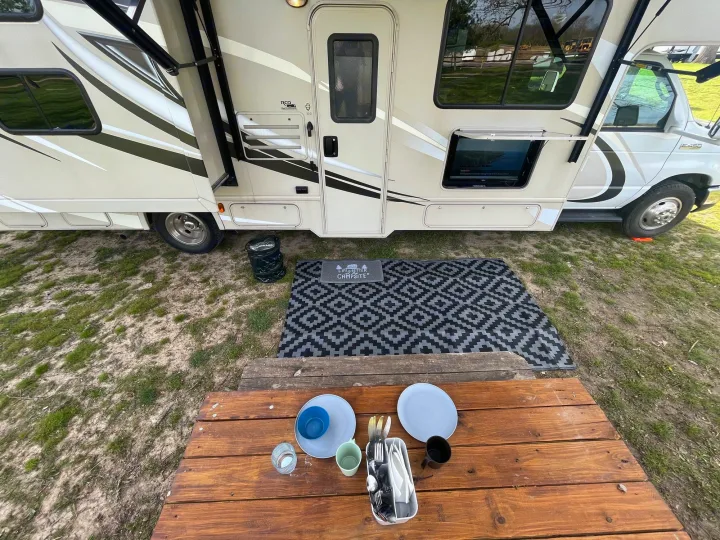 This RV rental campsite features an extended awning, outdoor TV, ground mat, and picnic table for comfortable outdoor living.. Thor Chateau 2017