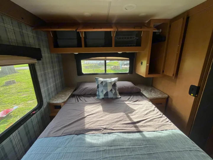 Cozy RV rental bedroom with a bed, overhead storage, and a scenic window view. Comfortable travel accommodations.. Thor Chateau 2017