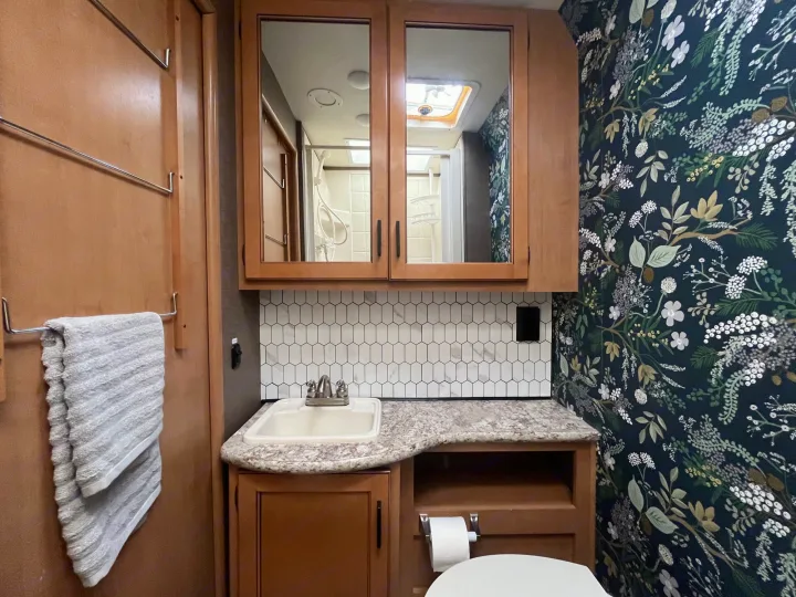 Step into this stylish RV rental bathroom! Features include floral wallpaper, hex tile backsplash, and a shower reflected in the mirror.. Thor Chateau 2017