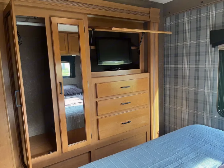 This RV rental bedroom provides efficient storage with a mirrored wardrobe, pop-up TV, drawers, and a cozy bed.. Thor Chateau 2017