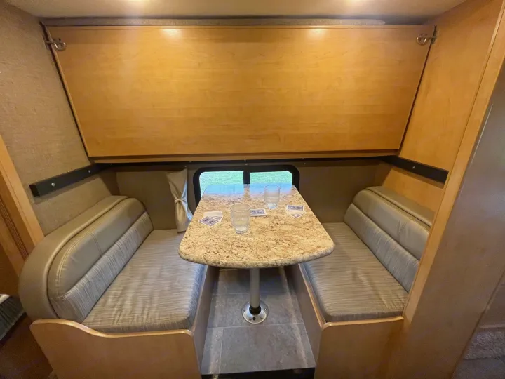 This RV rental's compact dinette features cozy booth seating, a table, and window view, perfect for games.. Thor Chateau 2017